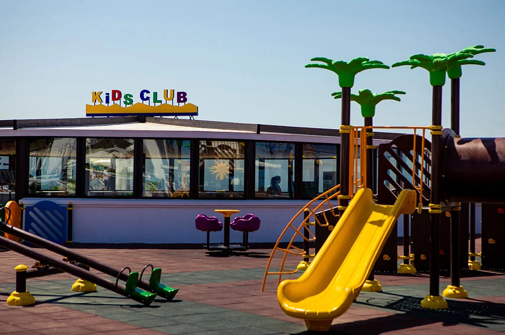Буквы KIDS CLUB на крыше павильона, рядом — горка и качели-балансир